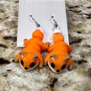 May include: A pair of orange fox dangle earrings with white tails and black eyes. The earrings are hanging from silver hooks.
