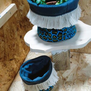 May include: Two blue fabric planters with white fringe trim. The top planter has a blue and yellow patterned fabric lining and holds two green succulents. The bottom planter is empty.