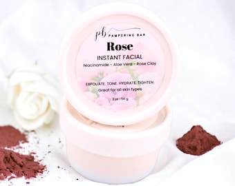 May include: A round, light pink container of Rose Instant Facial skincare product. The label features the text pb PAMPERING BAR, Rose, INSTANT FACIAL, Niacinamide - Aloe Vera - Rose Clay, EXFOLIATE. TONE. HYDRATE. TIGHTEN., and 2 oz | 56 g.