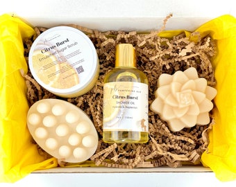 May include: A gift box filled with bath and body products, including a citrus-scented sugar scrub, shower oil, and two bars of soap. The box is lined with brown paper shreds and has a yellow tissue paper lining.