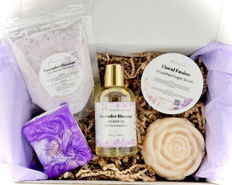 May include: A gift box filled with lavender-themed bath and body products. The box contains a lavender bath salt, a lavender shower oil, a lavender soap, a floral sugar scrub, and a rose-shaped candle.