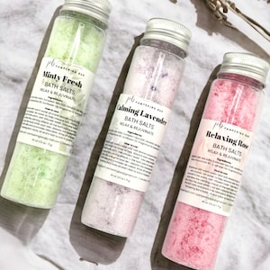 May include: Three small glass jars filled with bath salts. The jars are labeled "Minty Fresh", "Calming Lavender", and "Relaxing Rose". Each jar has a silver lid and a white label with black text.