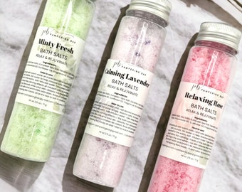 May include: Three small glass jars filled with bath salts. The jars are labeled "Minty Fresh", "Calming Lavender", and "Relaxing Rose". Each jar has a silver lid and a white label with black text.