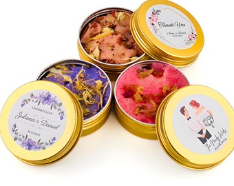 May include: Four gold metal tins with lids, each containing a different colored sugar scrub. The lids have personalized labels with floral designs and text that reads "Celebrate Love Juliana & Daniel 50.30.2020", "Thank You Clara & Daniel 12.12.2020", "The Next Chapter 02.06.2024", and a couple in wedding attire.