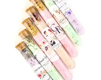 May include: Assortment of small glass tubes filled with bath salts and dried flowers. Each tube has a personalized label with a floral design and text such as "Thank You", "The Party Is On", "Bride Tribe", and "I'll You Be Me".