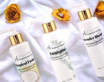 May include: Three white bottles of body lotion with gold lids and labels. The labels have a black and white design with the text "Pampering Bath" and the scent of each lotion: "Tropical Fusion", "Eucalyptus", and "Lavender Blossom".