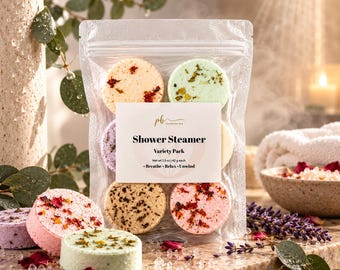 May include: A clear plastic pouch containing a variety pack of round shower steamers. The label reads Shower Steamer, Variety Pack, Net wt 1.5 oz | 42 g each, Breathe - Relax - Unwind. The steamers feature dried flower petals and herbs.