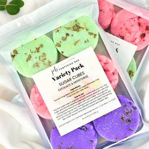 May include: A variety pack of sugar cubes for exfoliating and moisturizing skin. The cubes are in a clear plastic bag and are in different colors: green, pink, and purple. The bag has a label that says "Variety Pack Sugar Cubes Exfoliate & Moisturize" and lists the ingredients. The label also includes instructions on how to use the sugar cubes.