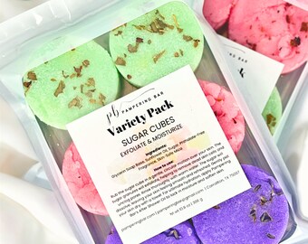 May include: A variety pack of sugar cubes for exfoliating and moisturizing skin. The cubes are in a clear plastic bag and are in different colors: green, pink, and purple. The bag has a label that says "Variety Pack Sugar Cubes Exfoliate & Moisturize" and lists the ingredients. The label also includes instructions on how to use the sugar cubes.