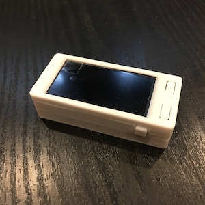 May include: A white rectangular device with a black screen and two buttons on the side.