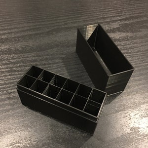 May include: Black plastic storage box with multiple compartments. The box is open and the compartments are visible.