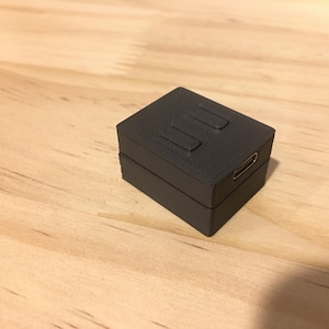 May include: A small, black, rectangular device with three buttons and a USB-C port.