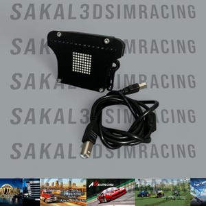 Może przedstawiać: Czarne urządzenie elektroniczne z siatką białych świateł, połączone z czarnym kablem USB. Urządzenie ma unikalny kształt i prawdopodobnie służy do gier lub symulacji. Tło zawiera tekst "SAKAL3DSIMRACING" w powtarzającym się wzorze.