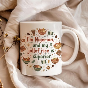 Peut inclure: Mug en céramique blanche avec une anse, portant l'inscription "I'm Nigerian, and my jollof rice is superior." Le motif comprend des illustrations de nourriture, un tambour et le drapeau nigérian. Le mug est posé sur un fond en tissu blanc.