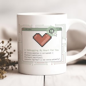 Może przedstawiać: Biały ceramiczny kubek z uchwytem, z pikselowym wzorem serca i napisem "Debugging My Heart For You". Projekt zawiera układ przypominający kod komputerowy z tekstem "LIVE 6885" na górze. Kubek ma czystą, nowoczesną estetykę.