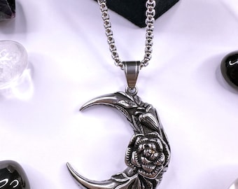 May include: A silver chain necklace with a crescent moon pendant featuring a detailed rose design.