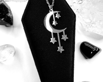 May include: A silver crescent moon necklace with dangling stars. The necklace is displayed in a black velvet coffin-shaped box.