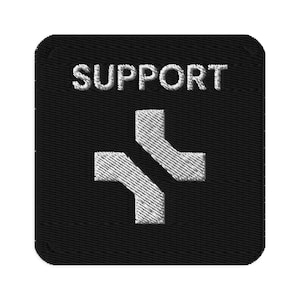 以下が含まれることがあります： 白の「SUPPORT」の文字が刺繍された黒い正方形のパッチ。白い様式化された十字のシンボルが上にあります。パッチは角が丸く、質感のある外観をしています。