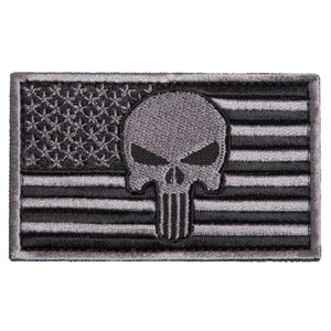 May include: A rectangular patch featuring a stylized American flag design in shades of gray. The flag's stars are visible in the upper left corner, and the stripes run horizontally. A skull graphic is centered on the patch.