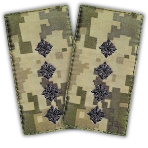 Könnte beinhalten: Zwei militärische Rangabzeichen. Jeder Aufnäher hat ein Tarnmuster in Grün-, Braun- und Beigetönen. Drei schwarze, gestickte rautenförmige Abzeichen sind auf jedem Aufnäher zentriert. Die Aufnäher sind rechteckig mit abgerundeten Ecken.