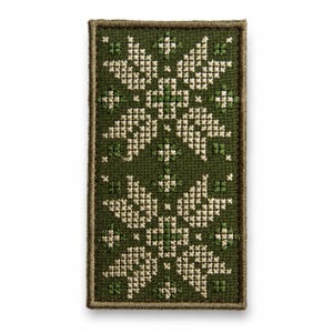 May include: A rectangular patch featuring a dark olive green fabric base with a symmetrical cross-stitch pattern in cream and light green thread. The design consists of two repeating floral-like motifs with a stitched border in olive green.