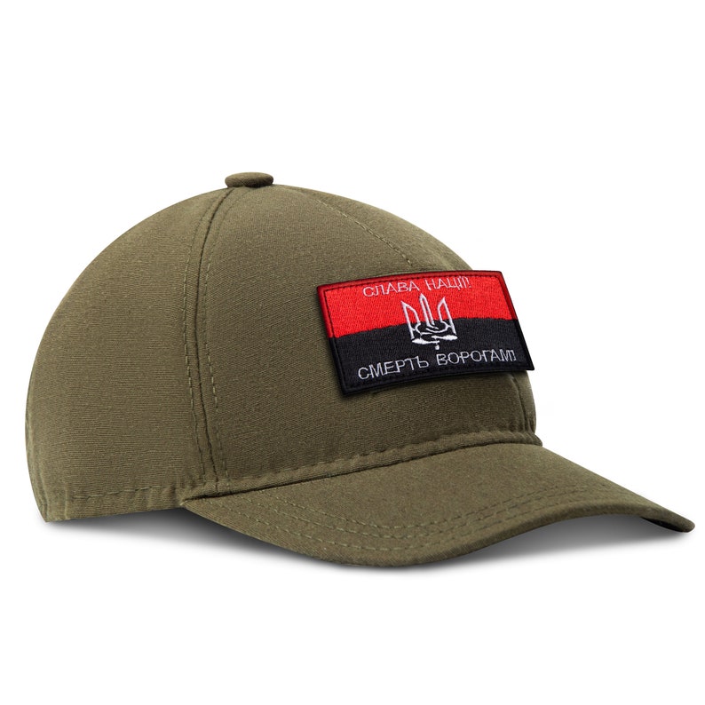 May include: An olive green baseball cap with a curved peak. A rectangular patch on the front displays a red and black design with white text and a trident symbol. The cap is made of a textured fabric.