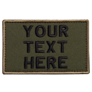 Puede incluir: Parche rectangular verde oliva con texto bordado en negro "YOUR TEXT HERE". El parche tiene un borde marrón y está diseñado para ser cosido o adherido a ropa o equipo.