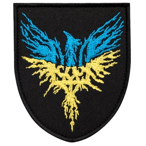 May include: Black embroidered patch featuring a stylized phoenix design in blue and yellow, set against a black shield-shaped background. The phoenix has outstretched wings and a detailed, textured appearance.
