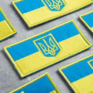 Op de afbeelding: Verschillende geborduurde patches met de Oekraïense vlag. Elke patch heeft een blauw bovenste gedeelte en een geel onderste gedeelte, met een gouden rand. Het Oekraïense wapen is in goud geborduurd.