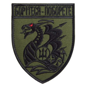 May include: Olive green embroidered patch with a black dragon design, a trident symbol, and the text "БОРІТЕСЯ-ПОБОРЕТЕ" in black. The dragon has a red eye. The patch is shield-shaped.