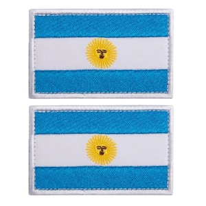 Op de afbeelding: Twee rechthoekige patches met de Argentijnse vlag. Elke patch heeft een lichtblauw en wit gestreept ontwerp met een geel zonne-embleem in het midden. De patches zijn omrand met witte stiksels.