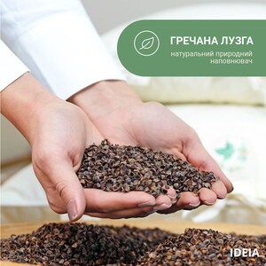 May include: Close-up of hands holding a pile of buckwheat hulls. The hulls are dark brown and appear to be a natural product. The image includes text in Ukrainian that translates to "buckwheat husk, natural natural filler."