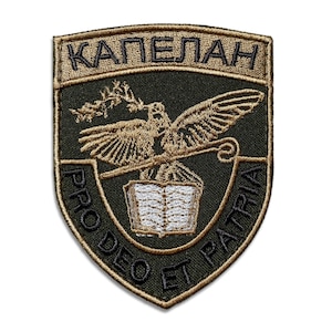 May include: Embroidered patch with a shield shape. The patch features a gold eagle holding a staff and olive branch over an open book. The text "КАПЕЛАН" is at the top, and "PRO DEO ET PATRIA" is around the bottom edge. The background is black.