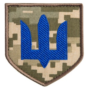 May include: A patch featuring a blue trident emblem, embroidered on a camouflage background. The patch has a brown border and a shield shape. The trident is a symbol of Ukraine.