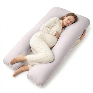 May include: A light gray U-shaped pregnancy pillow. The pillow is designed to support the body during sleep. The image shows a person wearing light-colored pajamas resting on the pillow. The pillow is made of a soft, plush material.