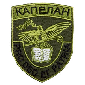 May include: An olive green embroidered patch with a shield shape. The patch features the word "КАПЕЛАН" at the top, an eagle with a book, and the text "PRO DEO ET PATRIA" in a curved banner.