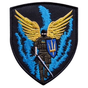 May include: Embroidered patch featuring a soldier with golden wings, a shield with a trident, and a sword. The design includes blue and yellow accents on a black background. The patch is shield-shaped.