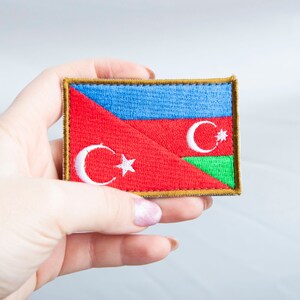 May include: A rectangular patch featuring the flag of Azerbaijan. The patch has a gold border and is divided into sections of blue, red, and green. White crescent moons and stars are visible on the red section.