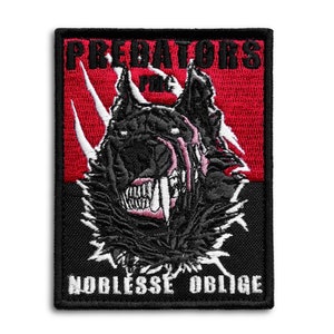 May include: Embroidered patch featuring a snarling wolf with sharp teeth and the text "PREDATORS" above and "NOBLESSE OBLIGE" below. The design incorporates red, black, and white colors, creating a striking contrast. The patch is rectangular with a black border.