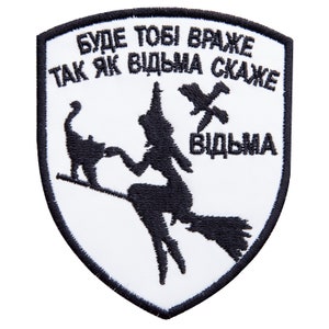 May include: A white patch with a black border featuring a witch on a broomstick, a cat, and text in Ukrainian. The witch is silhouetted, and the cat is perched on the broom. The text reads "Буде тобі враже так як відьма скаже" and "Відьма".