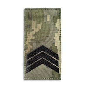Könnte beinhalten: Ein rechteckiger Militärpatch mit einem digitalen Tarnmuster in Grün-, Beige- und Grautönen. Drei schwarze Winkel sind unten prominent dargestellt und weisen auf den Rang hin. Der Patch hat einen genähten Rand.
