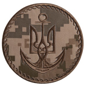 May include: Round patch featuring a brown anchor and trident emblem on a digital camouflage background. The emblem is outlined in brown, with a decorative rope-like border. The patch has a military or nautical theme.