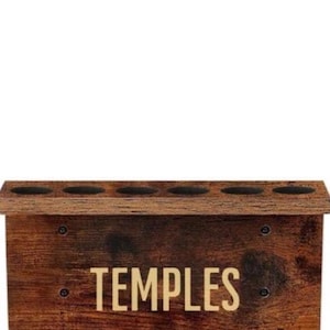 May include: A dark brown wood-grain finish wall-mounted organizer featuring the word TEMPLES in light-colored lettering. The unit includes a top shelf with six circular cutouts and a lower section with two black metal clips for holding items.