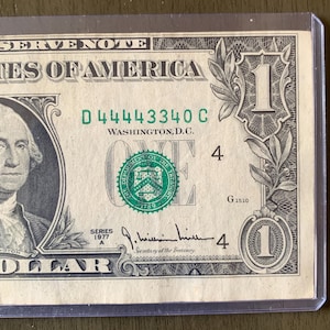 May include: A close-up of a one-dollar bill from the United States. The bill features a portrait of George Washington on the left and the number "1" in the corners. The bill is green and black with the text "ONE DOLLAR" and "WASHINGTON, D.C."
