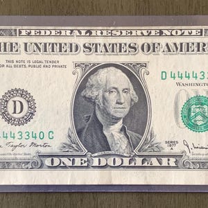 Puede incluir: Un billete de un dólar en una funda protectora. El billete presenta un retrato de George Washington y el texto "The United States of America". El billete es verde y negro con el número "1" en cada esquina.