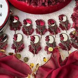May include: A collection of small, ornate, hand-held mirrors with a burgundy floral design. Each mirror has a small, round mirror with a bronze frame and a burgundy floral design. The mirrors are arranged on a white surface.