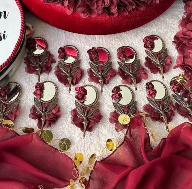 May include: A collection of small, ornate, hand-held mirrors with a burgundy floral design. Each mirror has a small, round mirror with a bronze frame and a burgundy floral design. The mirrors are arranged on a white surface.