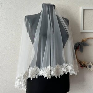 May include: A white bridal veil with a delicate lace trim. The veil is made of soft tulle and is perfect for a wedding ceremony or reception.