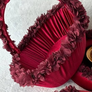 May include: A deep red velvet basket with a ruffled trim. The basket has a handle and is decorated with burgundy fabric flowers.