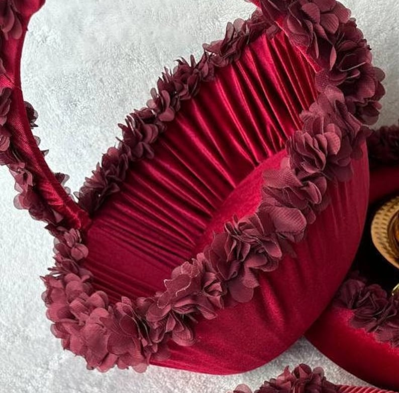 May include: A deep red velvet basket with a ruffled trim. The basket has a handle and is decorated with burgundy fabric flowers.
